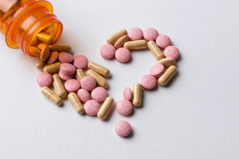 Pills and capsules arranged in heart shape on white surface from orange bottle