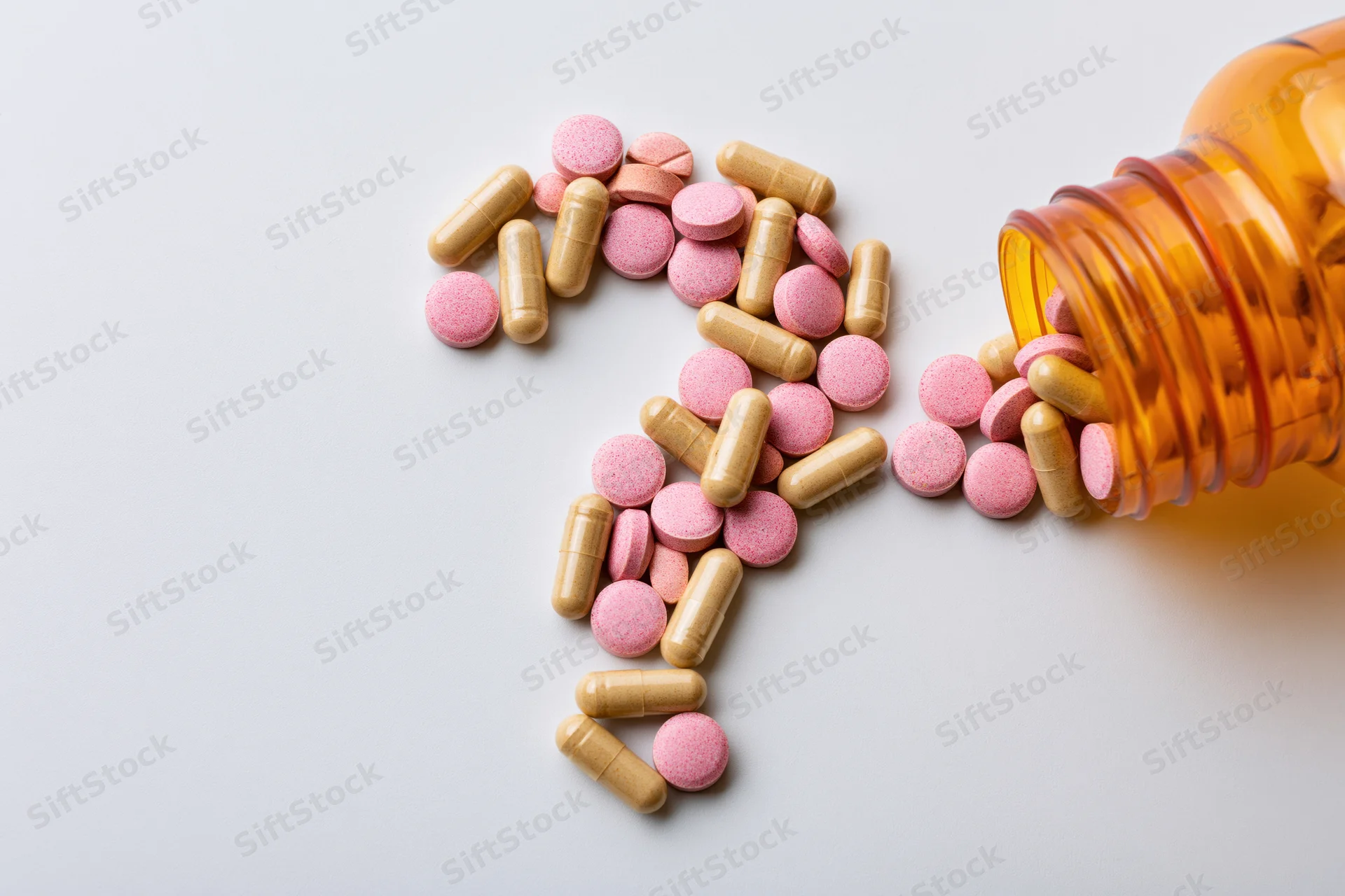 Assorted pills and capsules arranged in shape of question mark on white surface