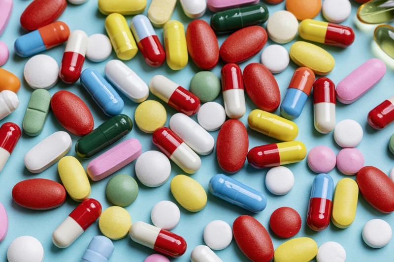 Assorted colorful pills and capsules scattered across a light blue surface