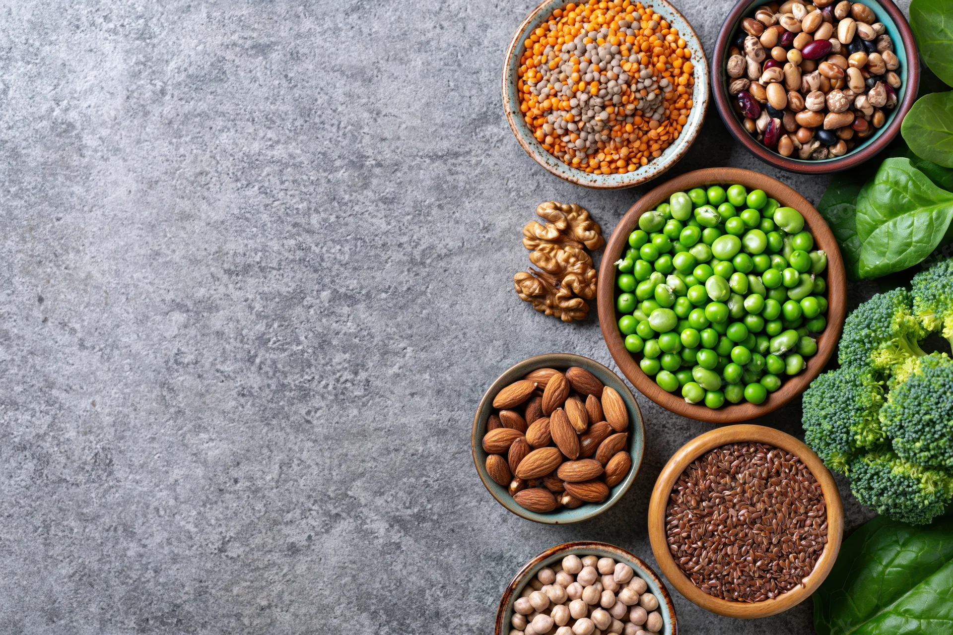 Assorted plant-based protein foods arranged in ceramic and wooden bowls on a gray countertop