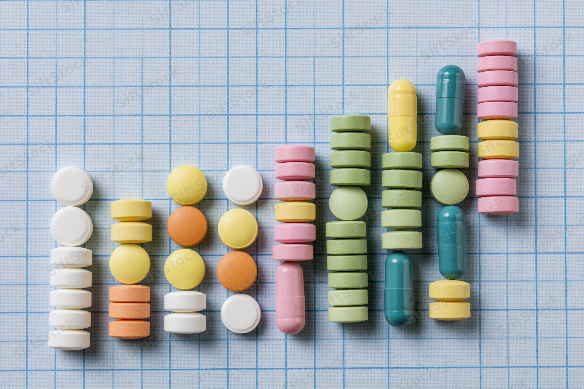Assorted medication pills and capsules arranged in rising columns on graph paper
