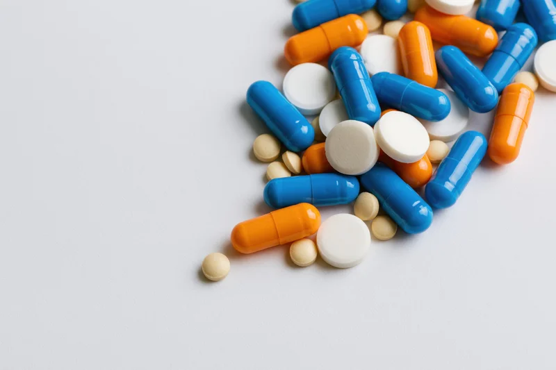 Assorted prescription pills and capsules scattered on a white surface