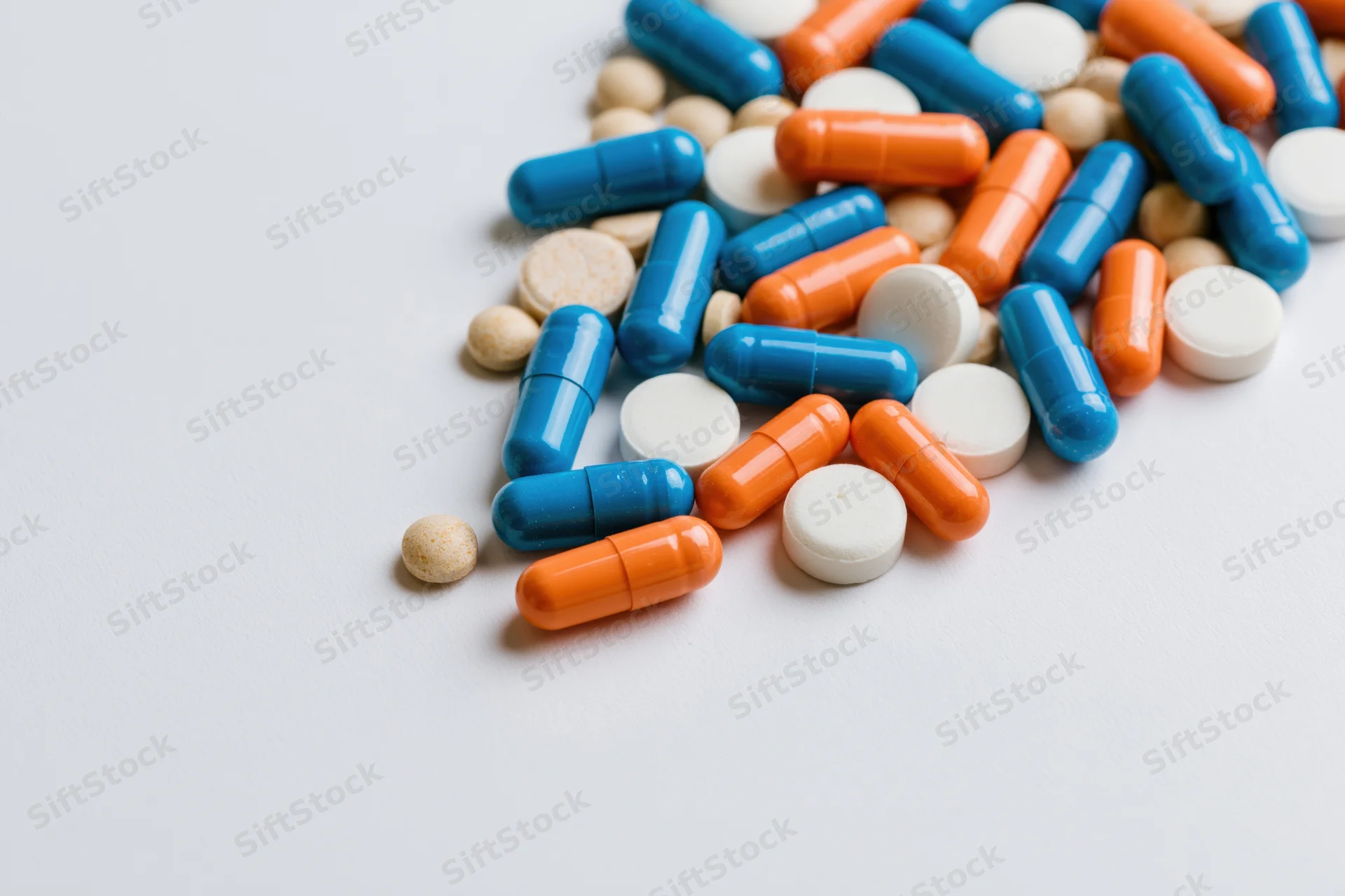 Assorted medication capsules and tablets scattered on a white surface