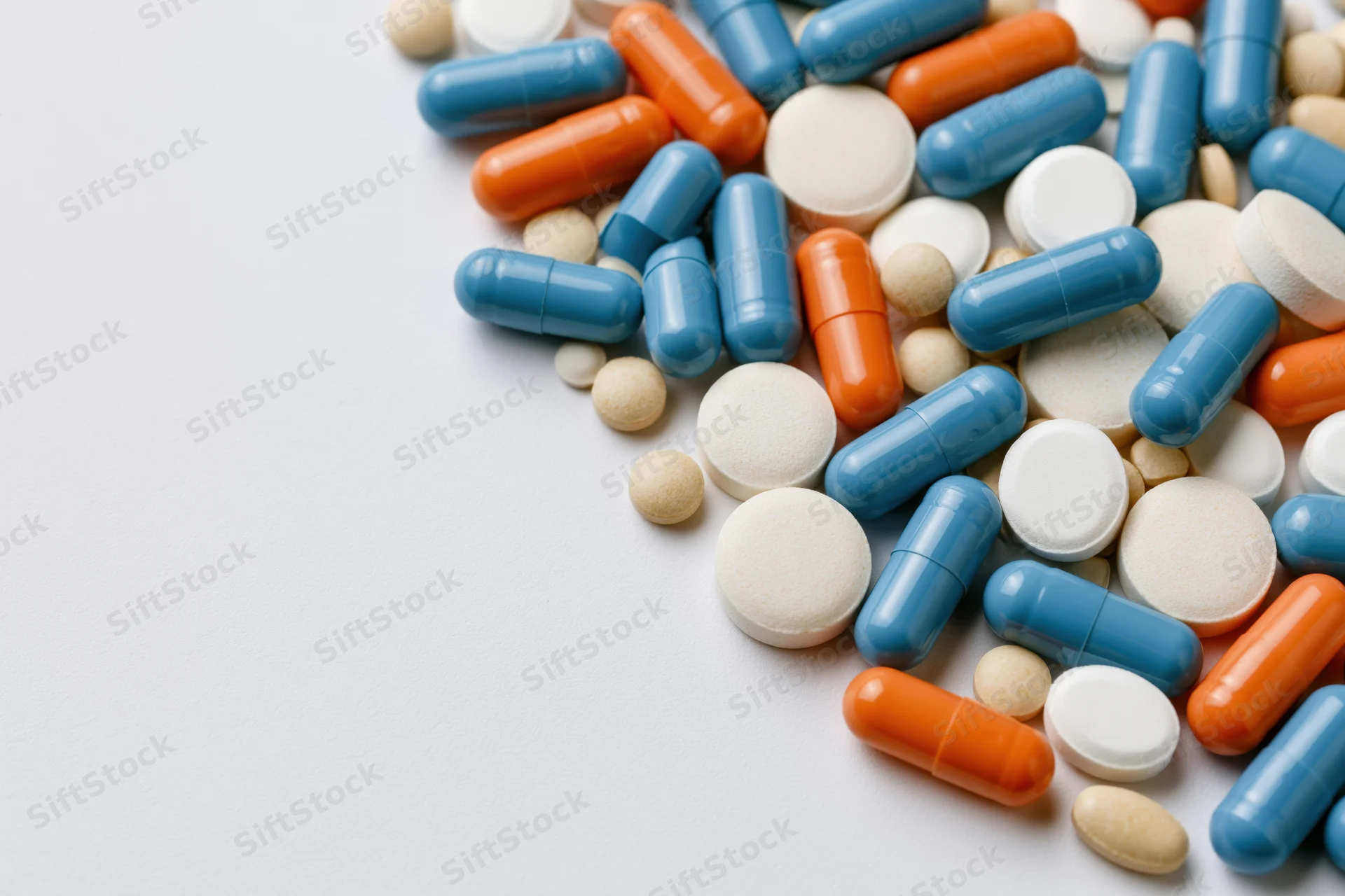 Assorted medication pills and capsules scattered on white surface with copyspace
