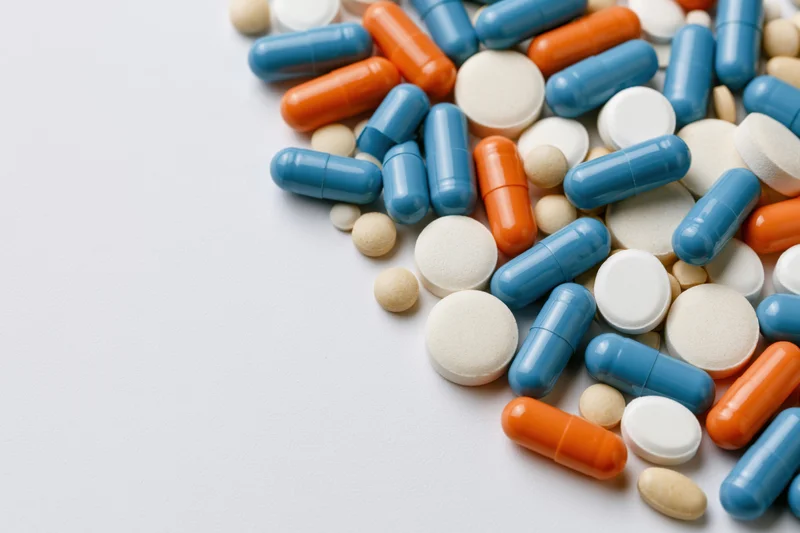 Assorted medication pills and capsules scattered on white surface with copyspace