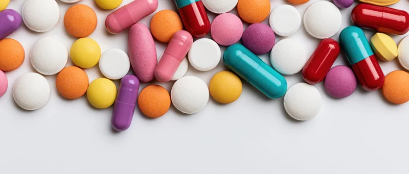 Assorted colorful pills and capsules scattered on white surface with copyspace