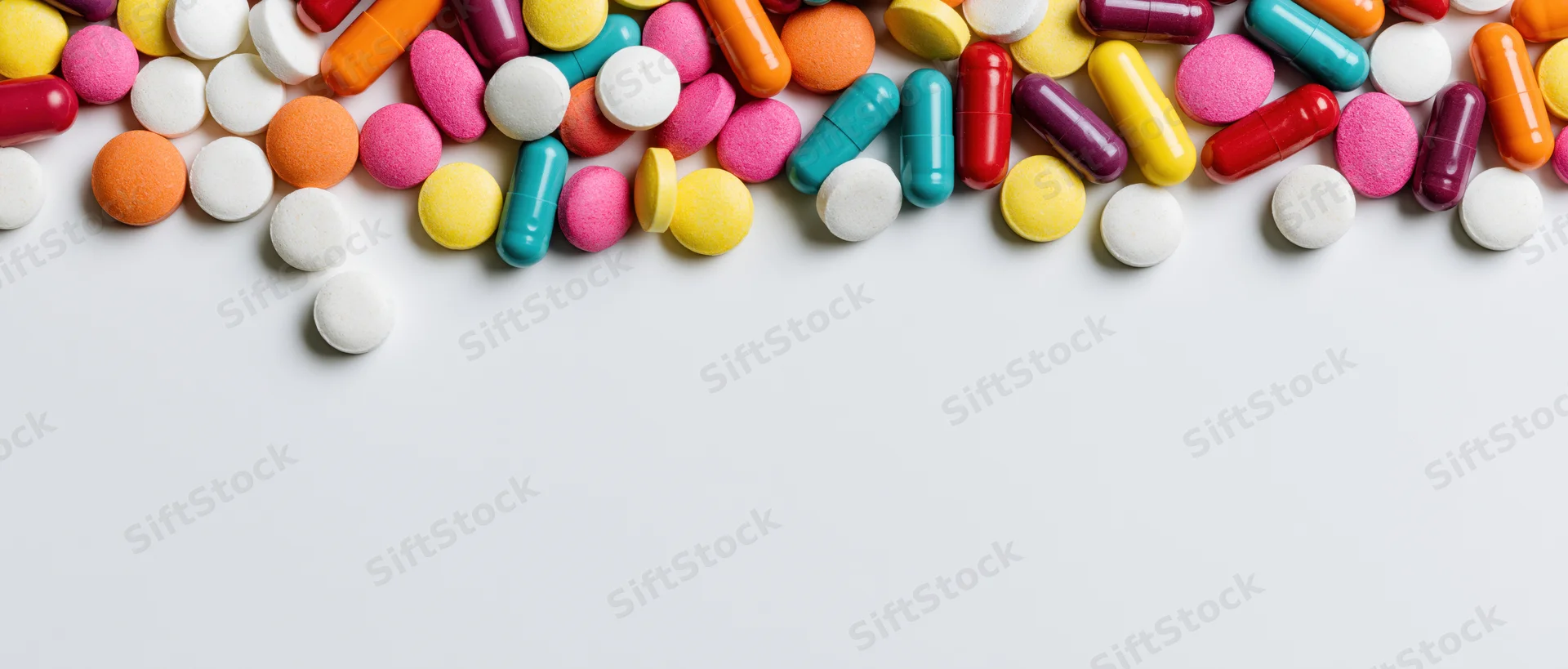 Assorted colorful pills and capsules scattered across white surface with copyspace below