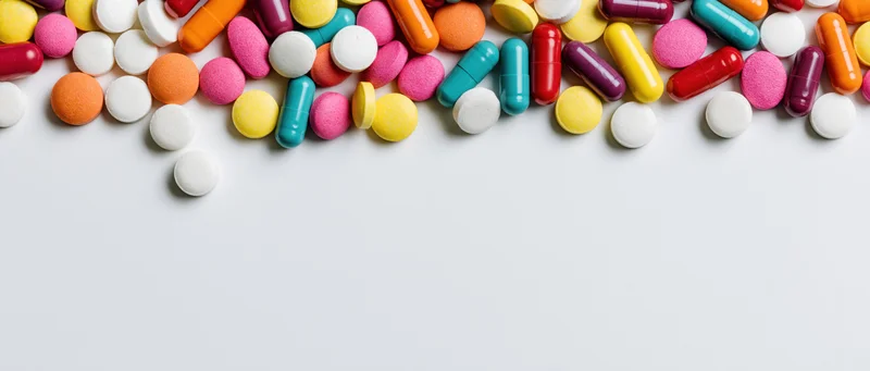 Assorted colorful pills and capsules scattered across white surface with copyspace below
