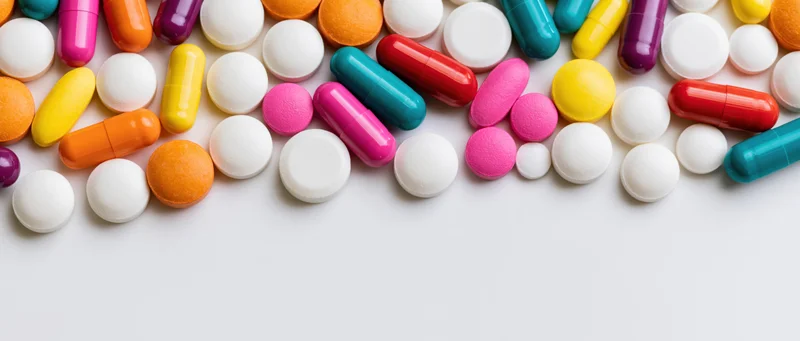 Assorted colorful pills and capsules scattered loosely on white surface with copyspace below