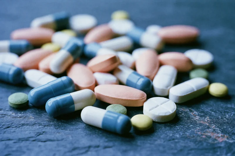 Assorted prescription pills and capsules scattered on a dark stone surface