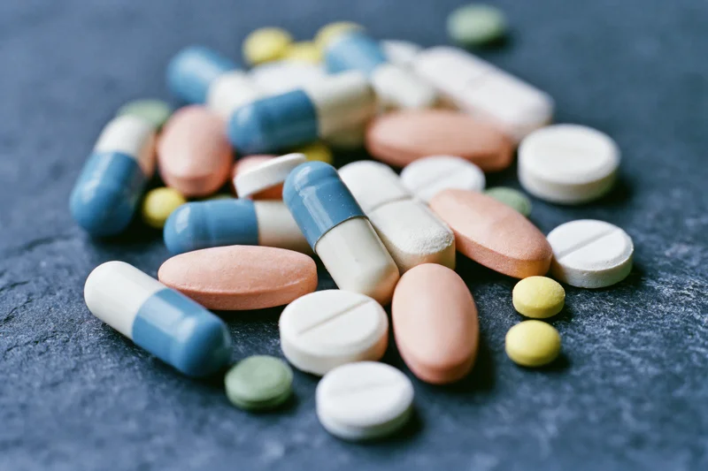 Assorted prescription pills and capsules scattered loosely on a dark textured surface