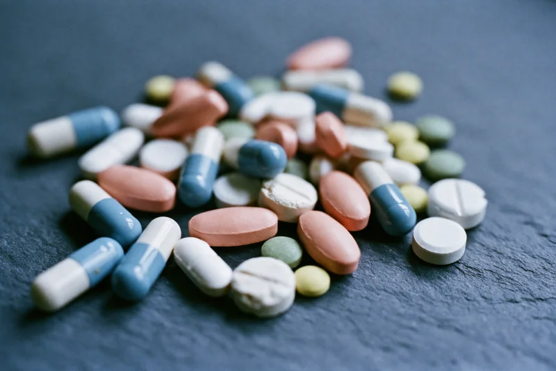 Assorted prescription pills and capsules scattered on a dark slate surface