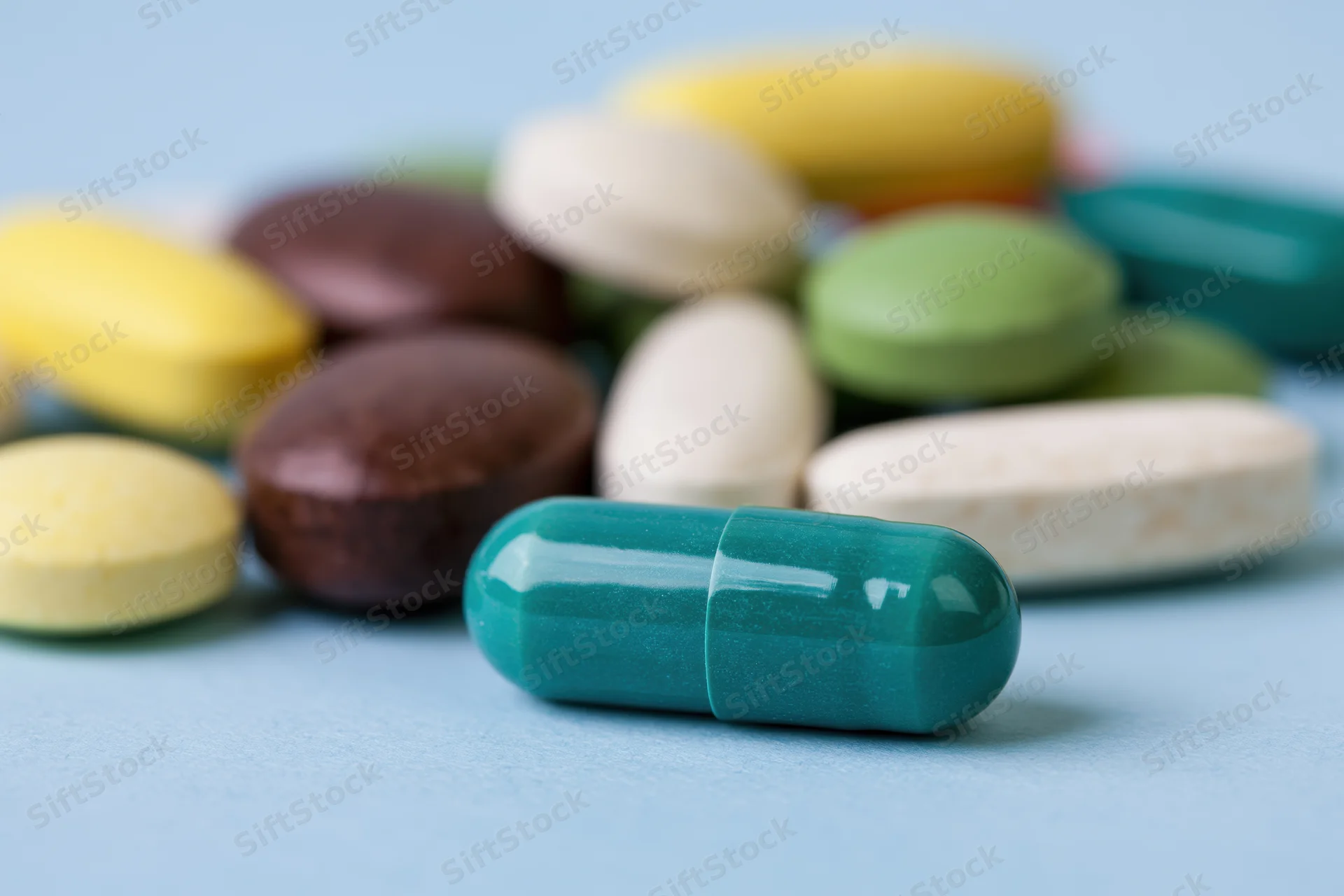 Assorted colorful pills and capsules scattered on a light blue surface