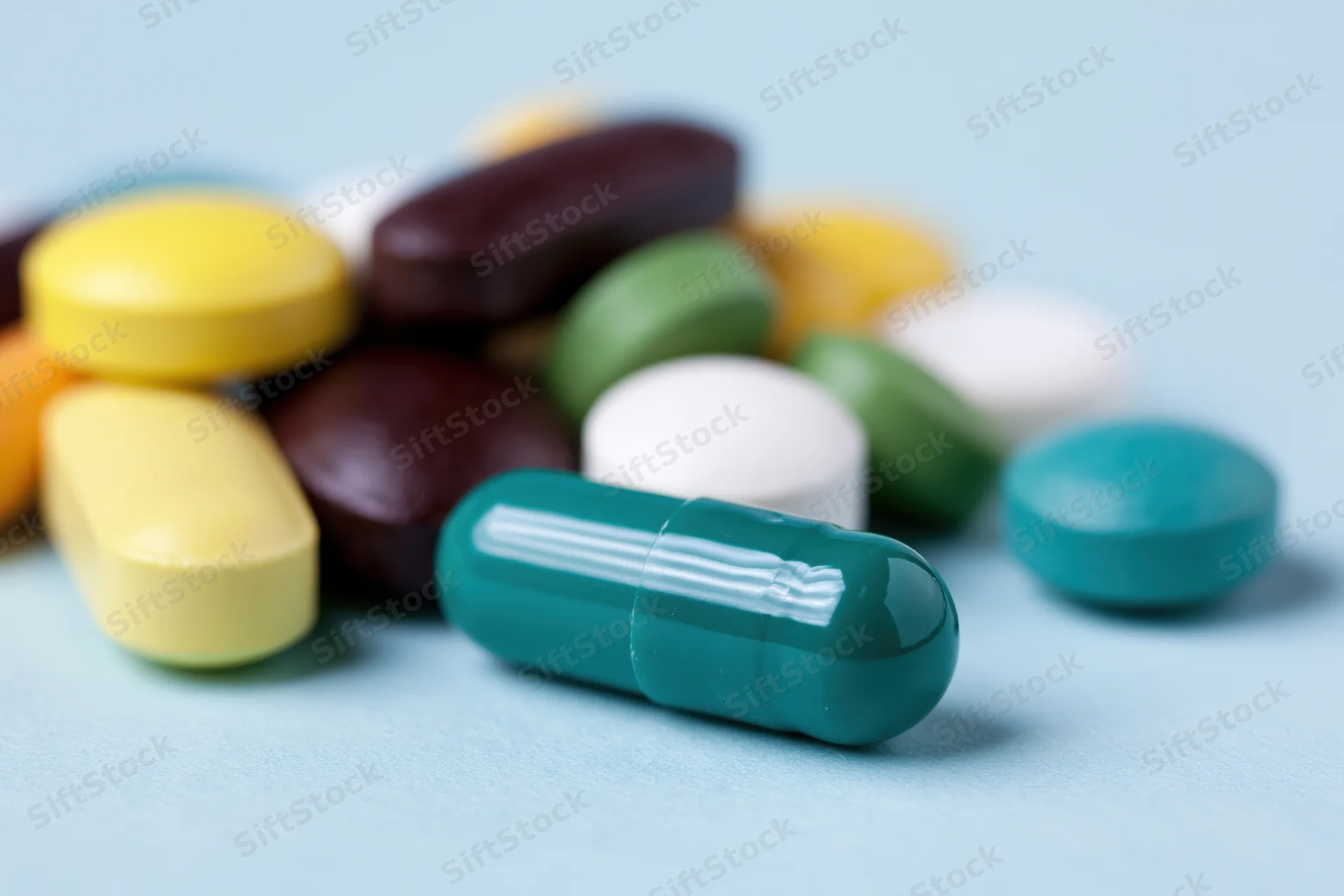 Assorted prescription pills and capsules scattered on a light blue surface