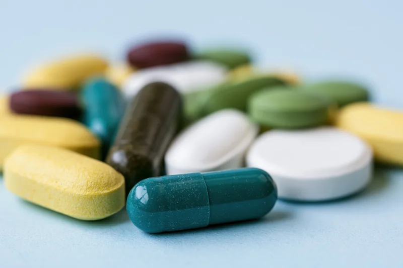 Assorted medication pills and capsules scattered on a light blue surface