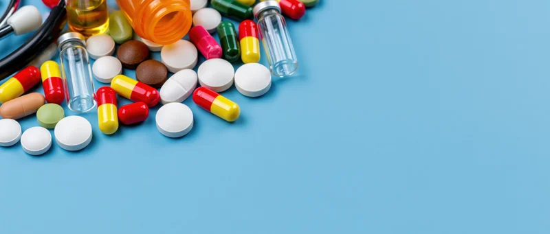 Assorted pills and capsules with medicine bottles on a blue surface