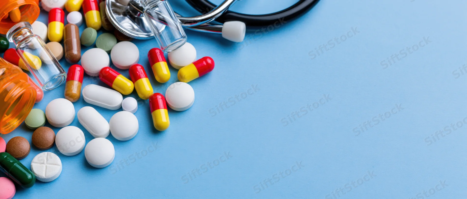 Assorted medicine pills and capsules with stethoscope and glass bottles on blue surface