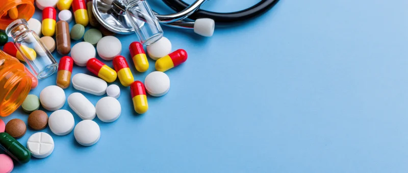 Assorted medicine pills and capsules with stethoscope and glass bottles on blue surface