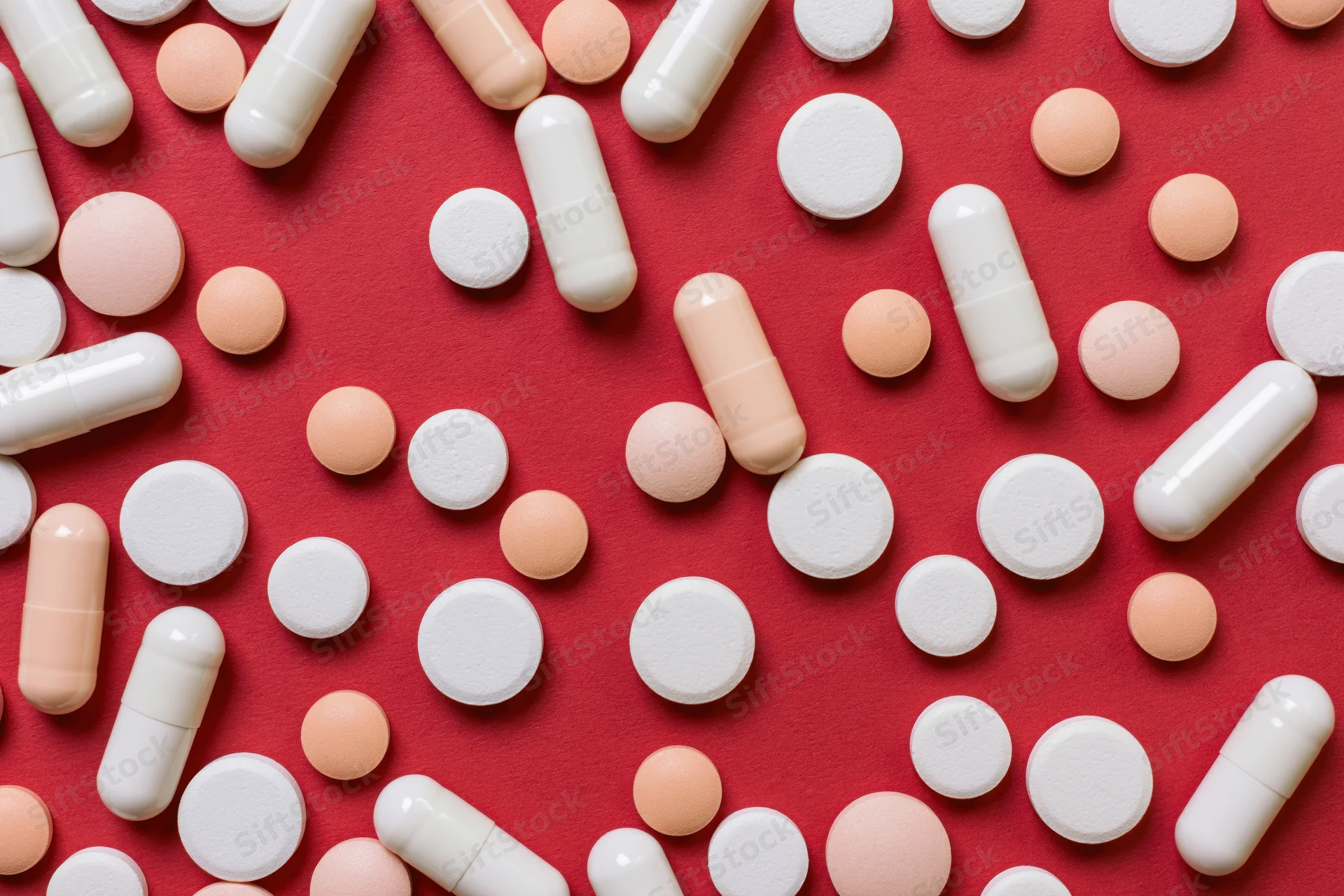Assorted white and orange pills scattered on red surface