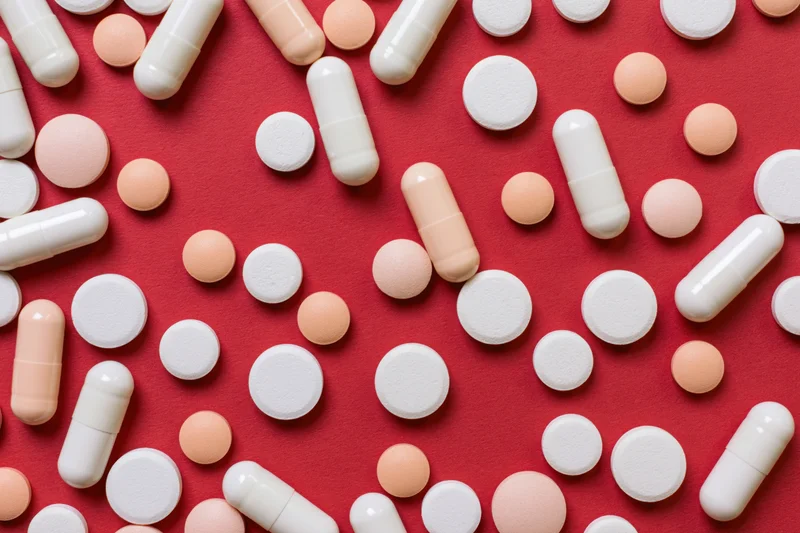 Assorted white and orange pills scattered on red surface