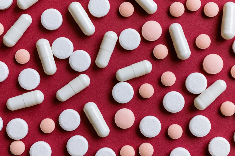 Assorted white capsules and round tablets scattered on a red surface