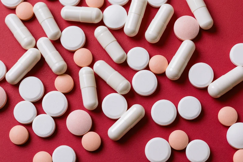 Assorted white capsules and round tablets scattered on a red surface