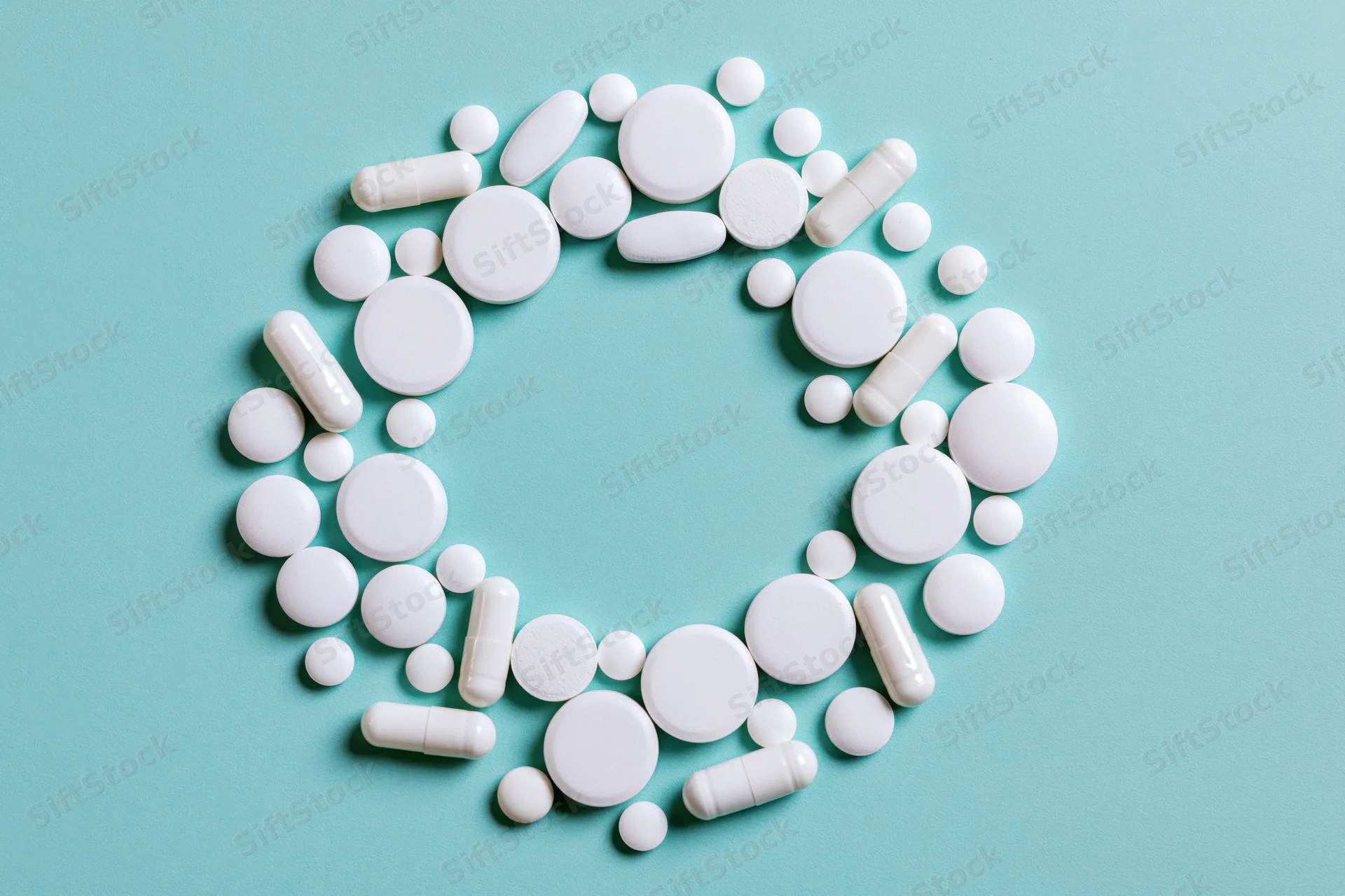 White pharmaceutical pills and capsules arranged in a circular pattern on a blue background