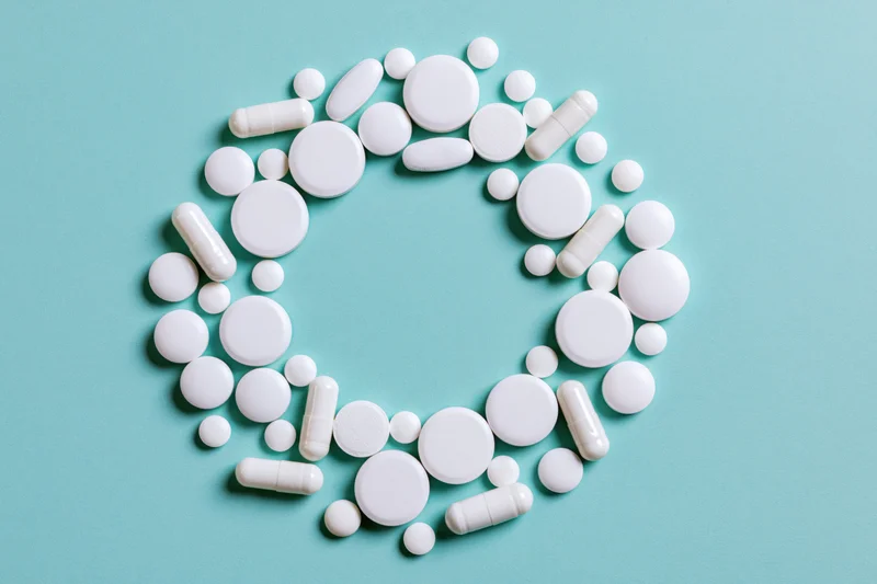 White pharmaceutical pills and capsules arranged in a circular pattern on a blue background