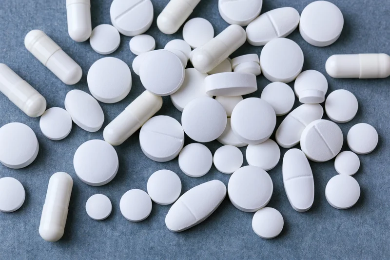 Assorted white pharmaceutical pills and capsules scattered on a textured blue surface