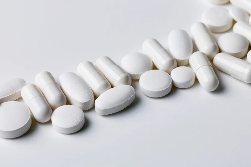Assorted white pharmaceutical pills and capsules scattered on a plain white surface