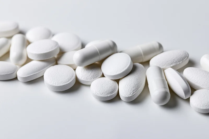 Assorted white pharmaceutical pills and capsules scattered on a plain white surface