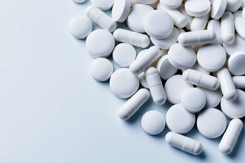 White pharmaceutical pills and capsules scattered on a light surface with copyspace