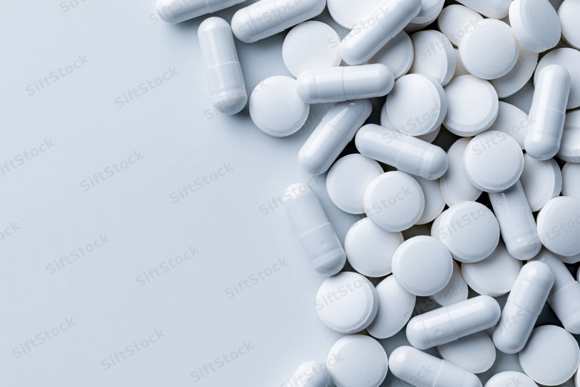 White pharmaceutical pills and capsules scattered on a light surface with copyspace