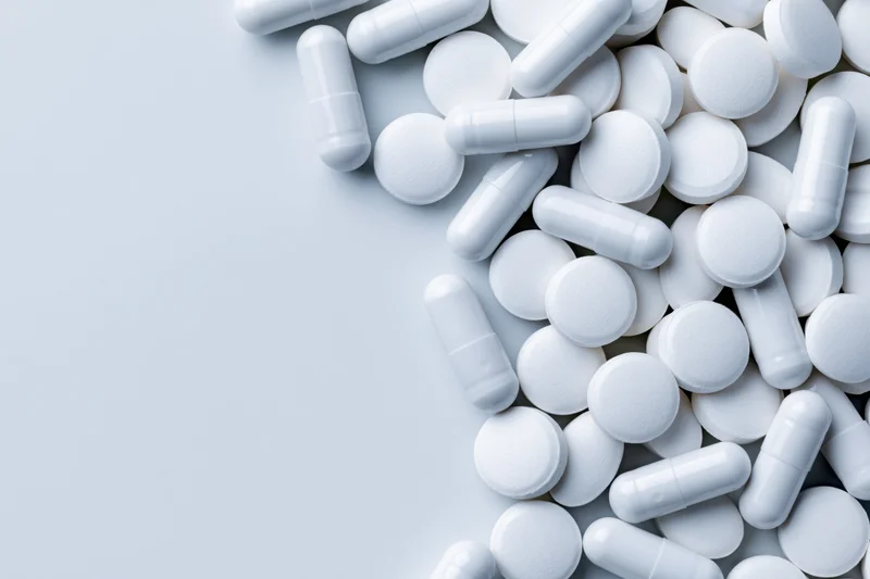 White pharmaceutical pills and capsules scattered on a light surface with copyspace