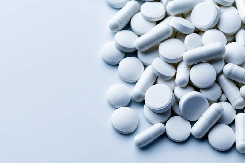 White pharmaceutical pills and capsules scattered on a light surface with copyspace
