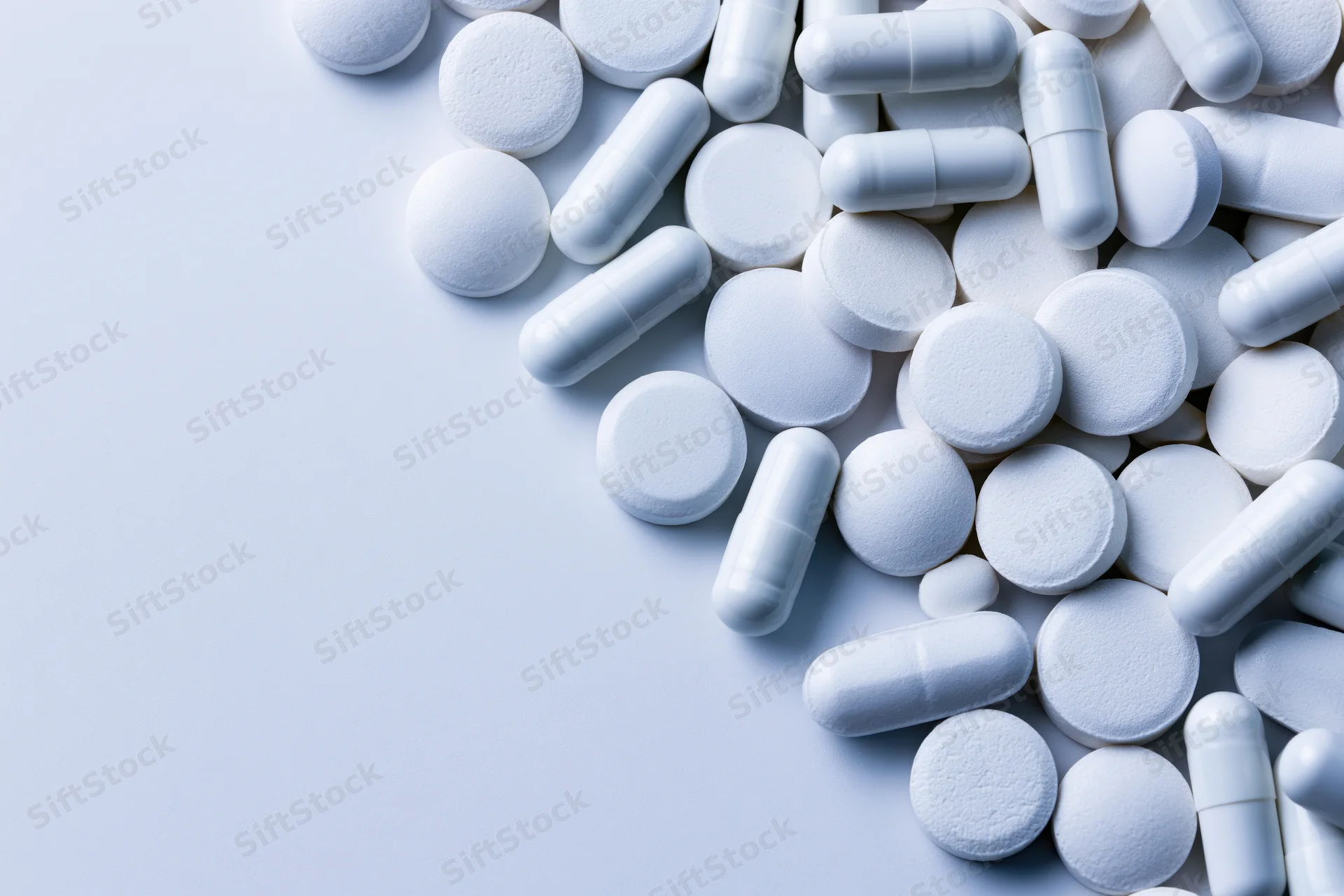 White pharmaceutical pills and capsules scattered on a light surface with copyspace