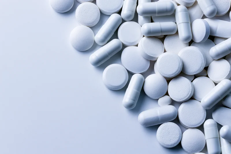 White pharmaceutical pills and capsules scattered on a light surface with copyspace