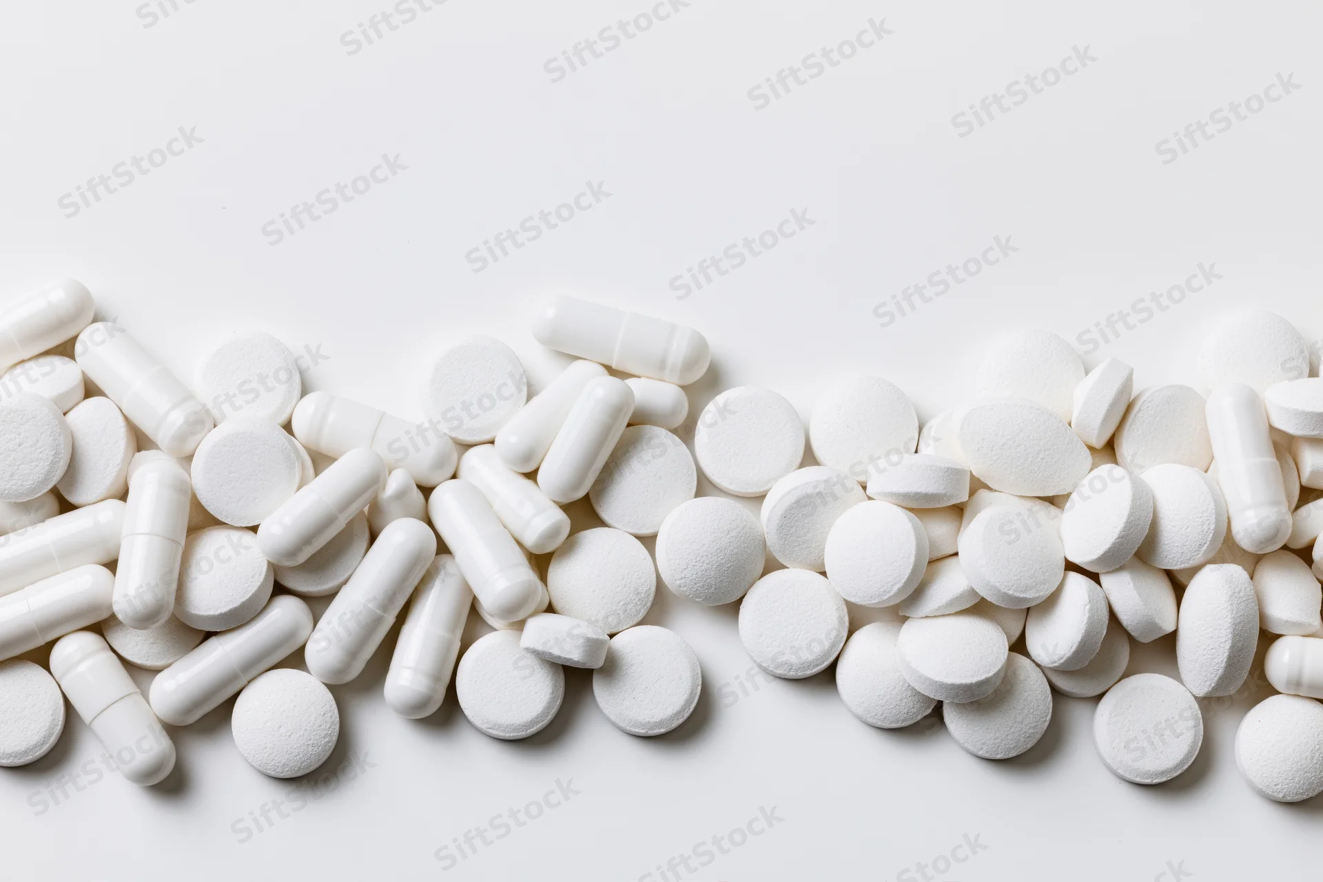 White pharmaceutical pills and tablets scattered across a plain white surface