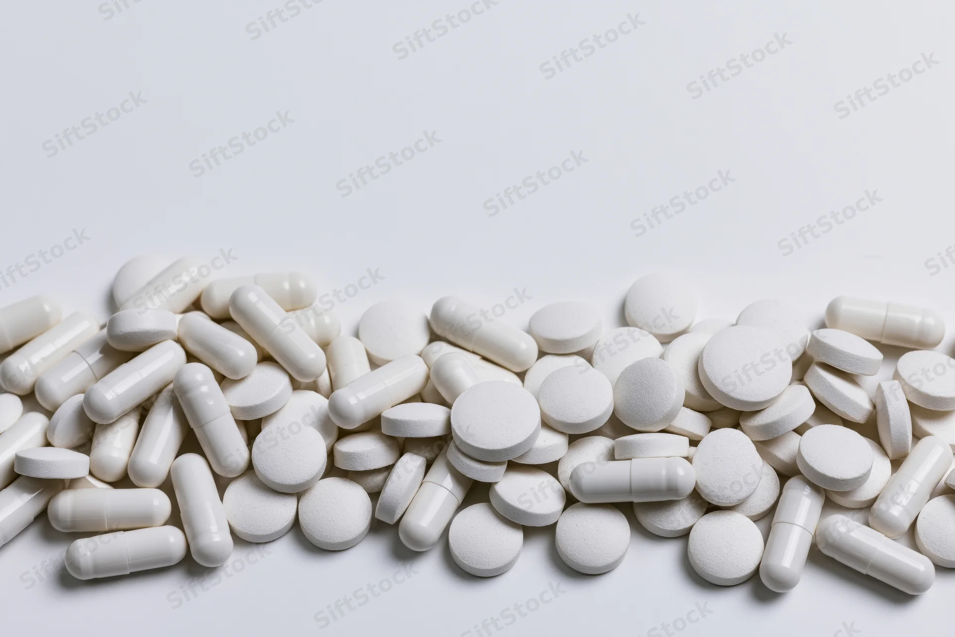 White pharmaceutical pills and tablets scattered across a plain white surface