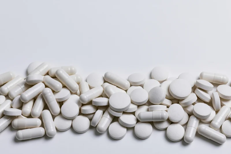 White pharmaceutical pills and tablets scattered across a plain white surface