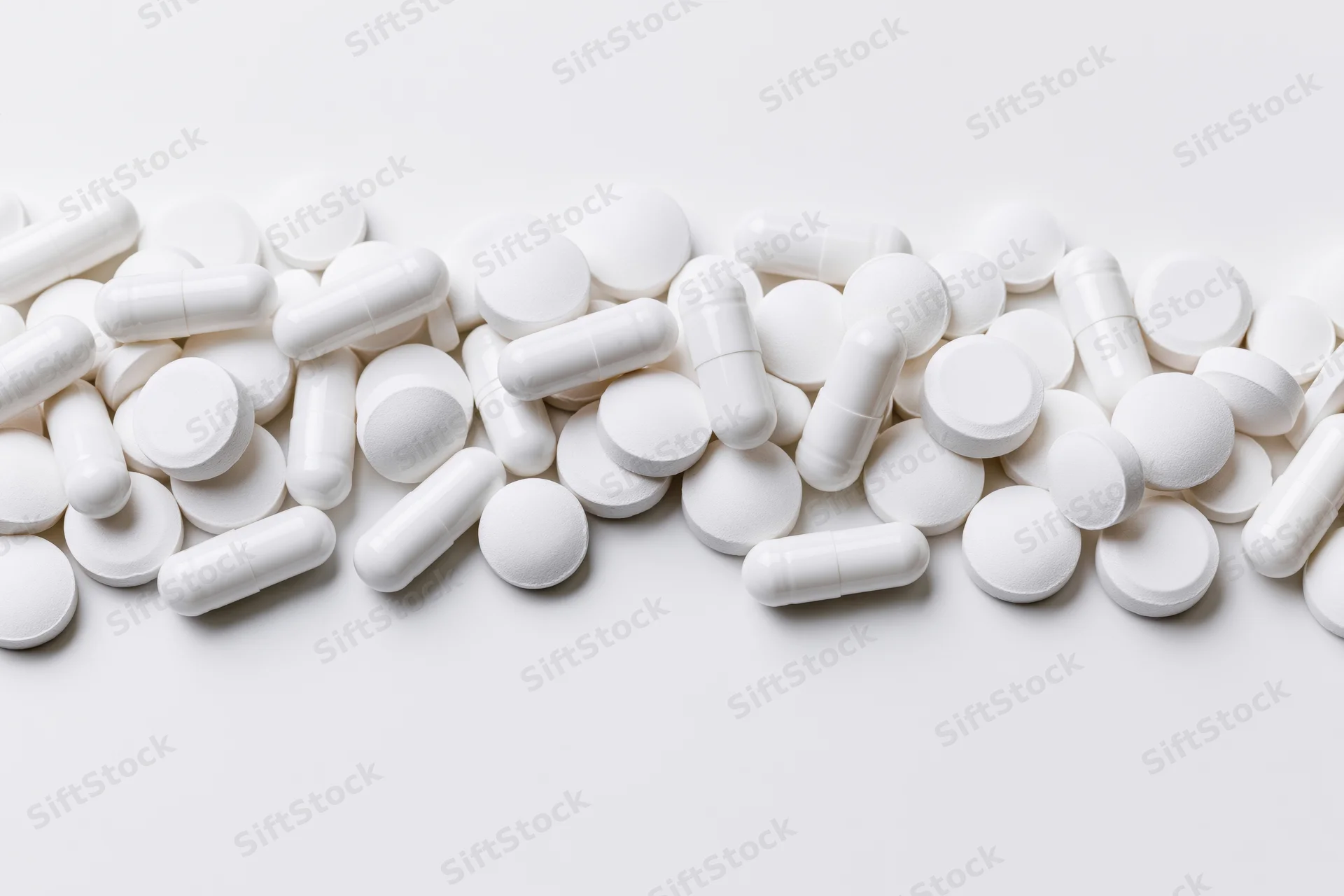 White pharmaceutical pills and capsules scattered across a plain white surface with copyspace below