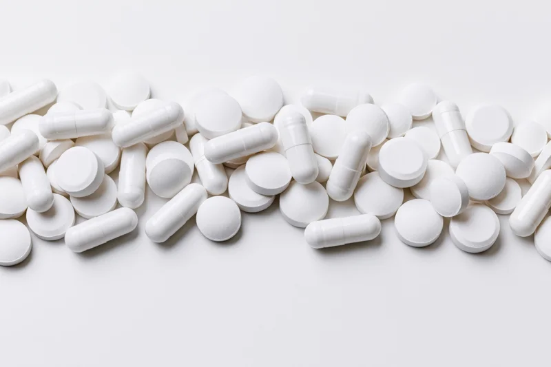 White pharmaceutical pills and capsules scattered across a plain white surface with copyspace below
