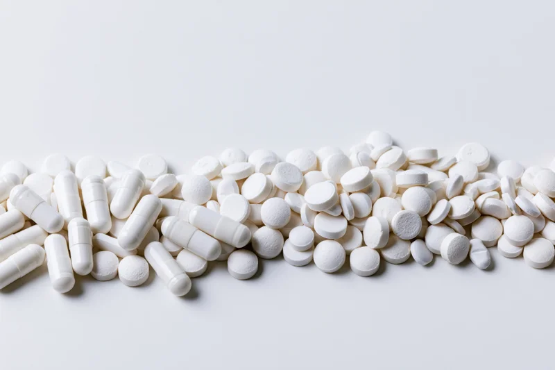 White pharmaceutical pills and tablets scattered across a plain surface