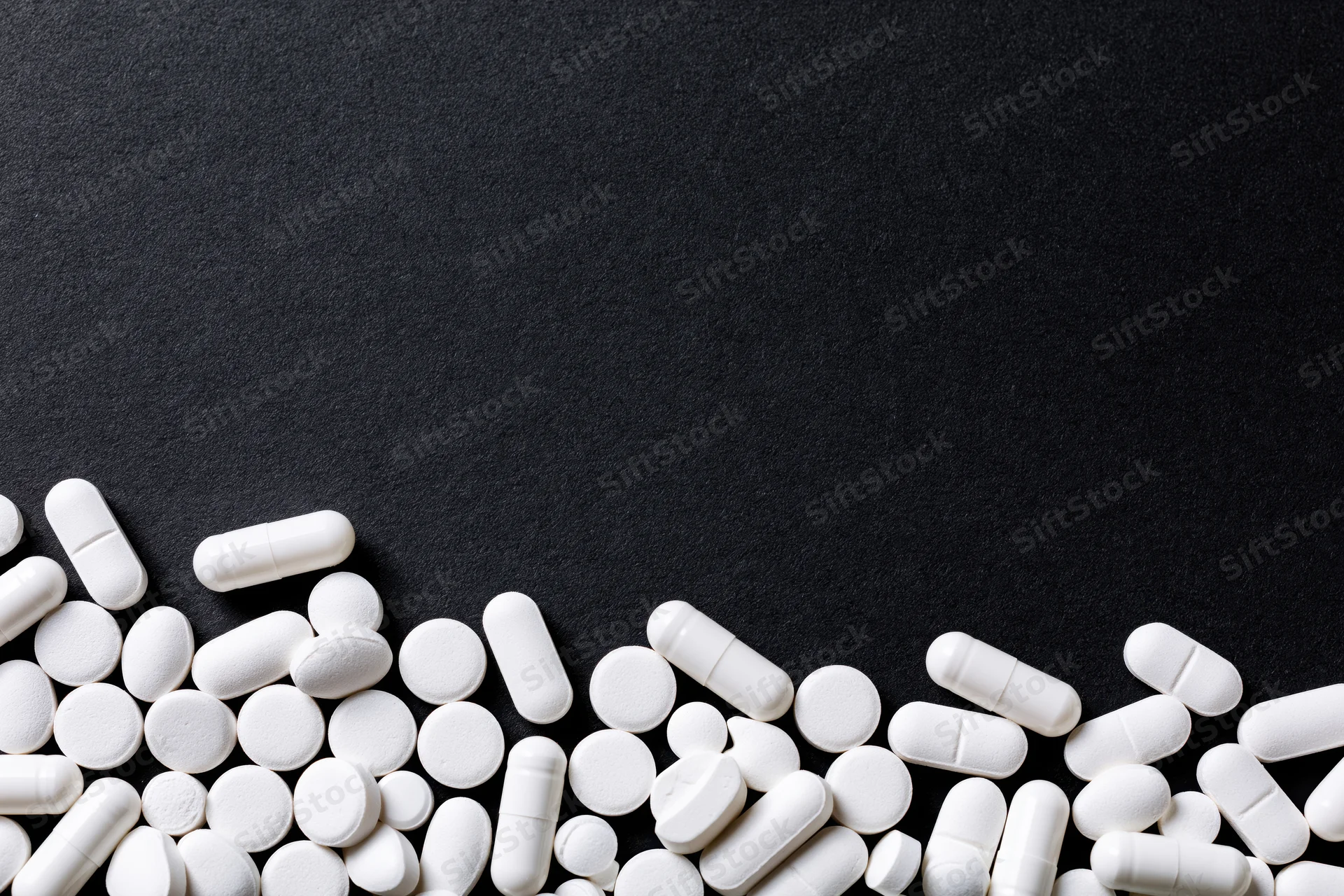 White tablets and capsules scattered along the bottom edge of a black surface