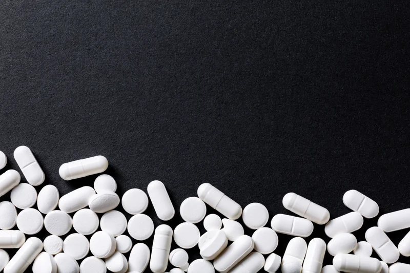 White tablets and capsules scattered along the bottom edge of a black surface