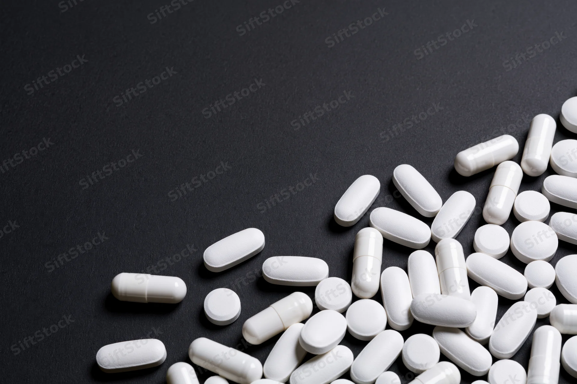 White pills capsules and tablets scattered on black surface with copyspace