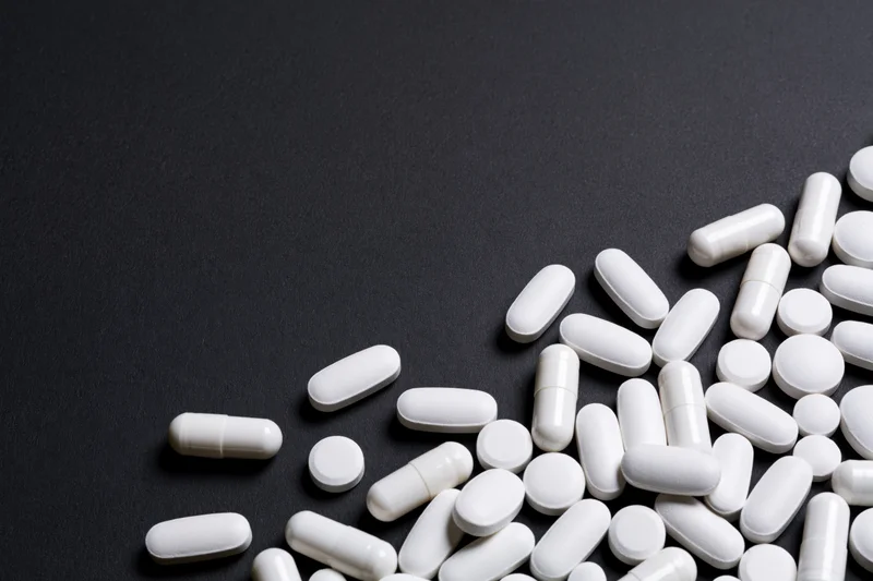 White pills capsules and tablets scattered on black surface with copyspace