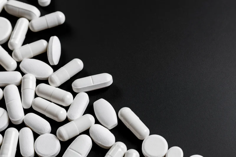White pills and capsules scattered loosely on black surface with copyspace