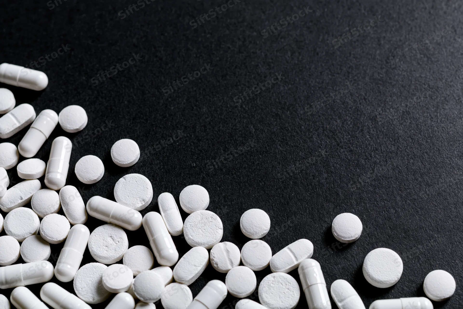 White tablets and capsules scattered loosely on dark surface