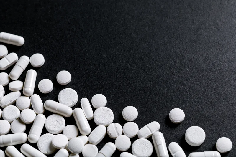 White tablets and capsules scattered loosely on dark surface